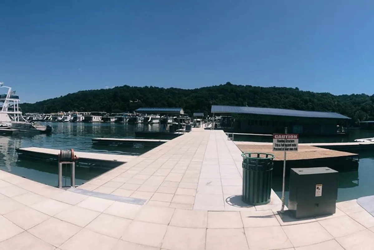 This image captures the vibrant scene at Pates Ford Marina, showcasing marina docks lined with boats against a backdrop of rolling green hills. The relaxed atmosphere is enhanced by the presence of people enjoying boating, fishing, and possibly preparing for a lakeside picnic. The waterside setting and communal feel reflect the marina’s role as a hub for aquatic adventure and leisure.
